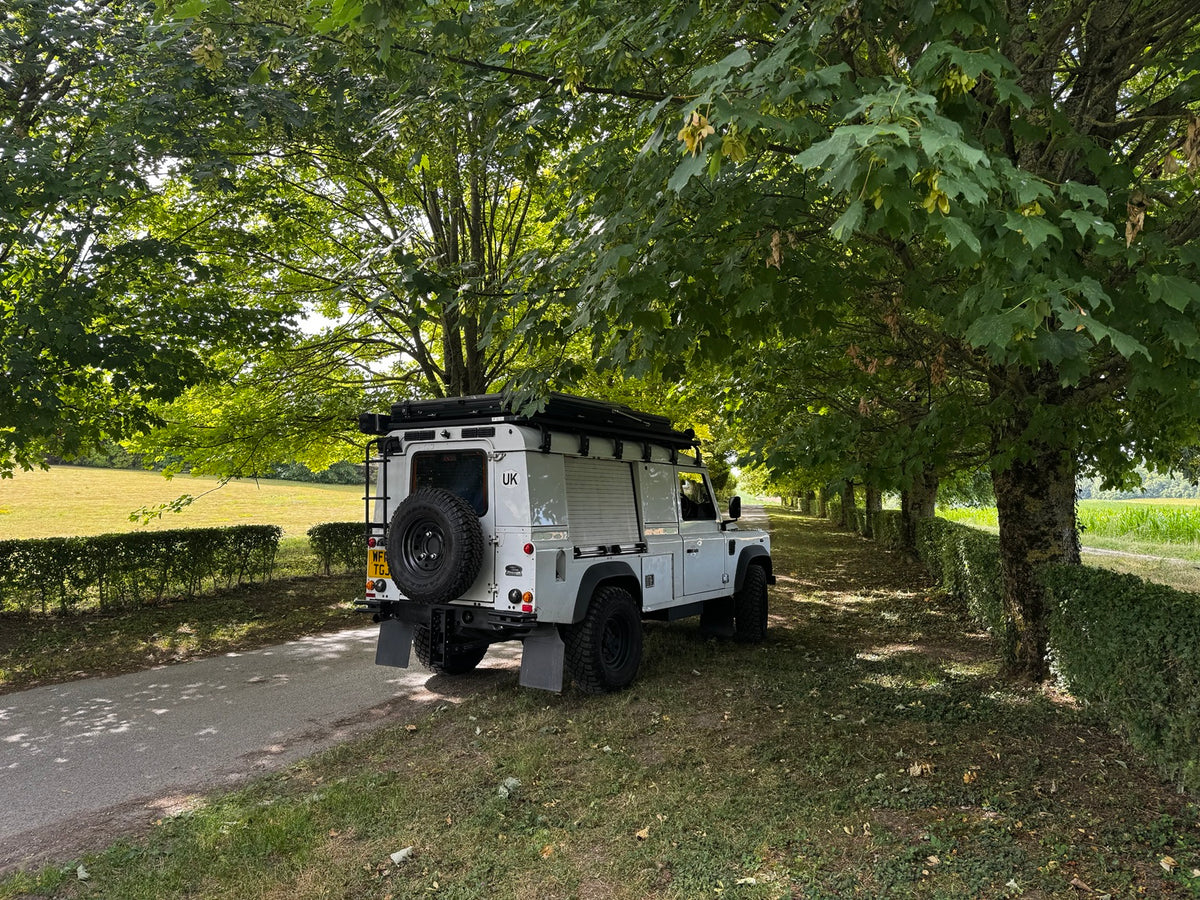 White Land Rover Defender expedition touring build beneath mature trees